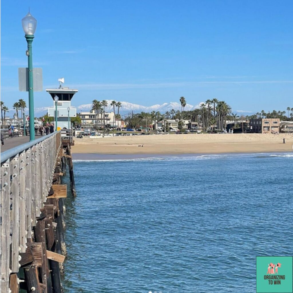 Seal Beach pier and blue ocean in the foreground. Beach and snow-capped mountains in the background