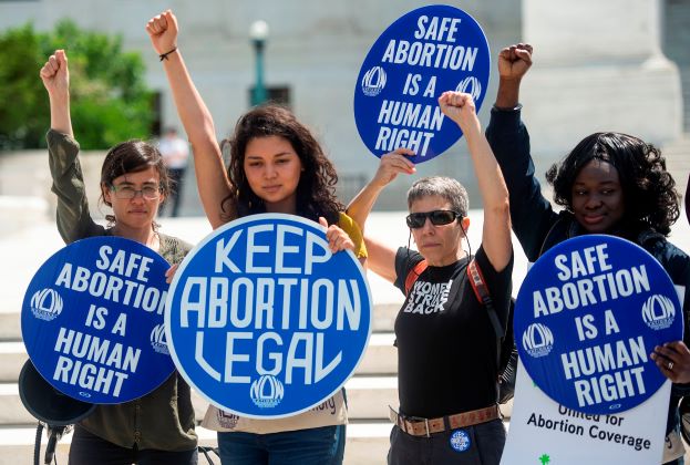 four women holding blue abortion rights signs with fists raised in the air