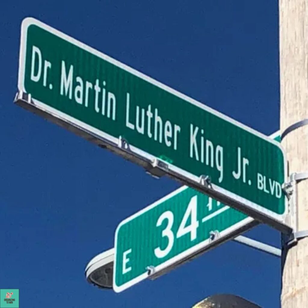 Street sign at the intersection of Dr. Martin Luther King Jr. blvd and East 34th St. The street signs are fastened to a wooden pole with metal strips. There is also a street light attached to the pole. Blue sky in the background.